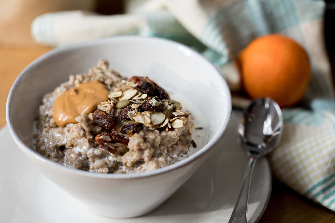 A bowl of Michele's Toasted Muesli topped with nuts and dried fruit, served with a spoon and an orange in the background.