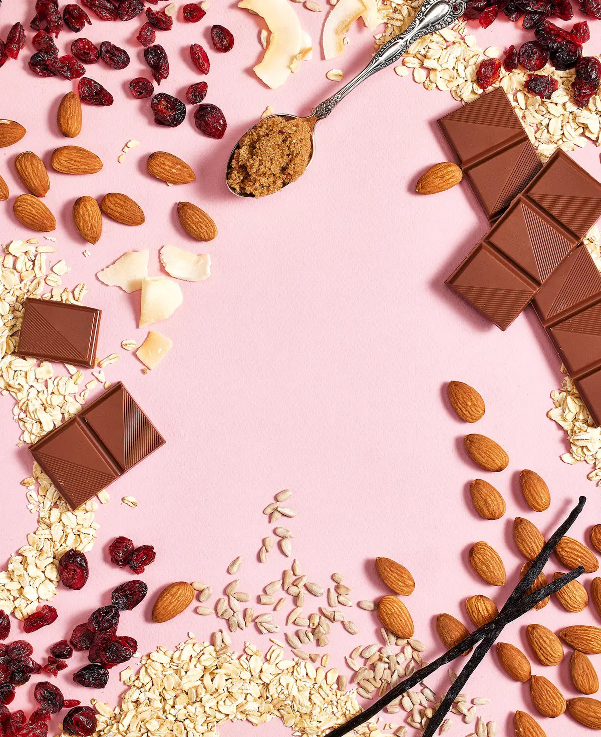 Michele's Granola chocolate pieces, almonds, dried cranberries, and vanilla beans on a pink background