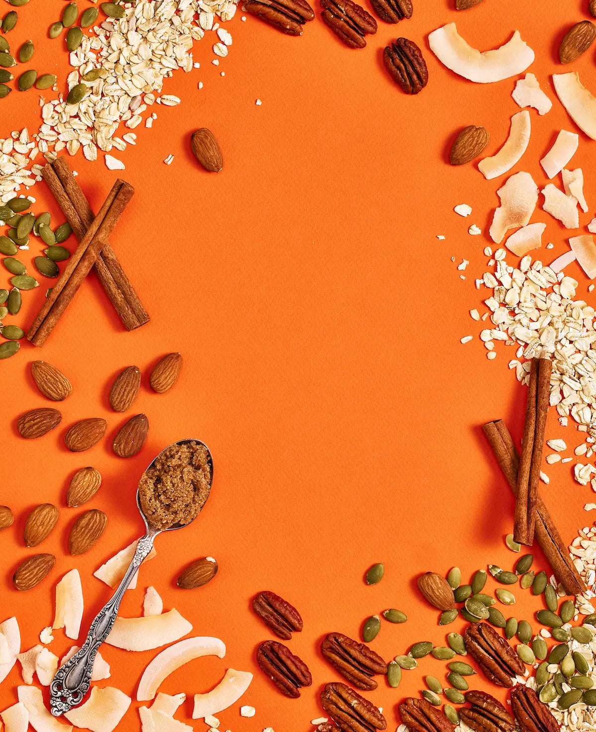 Michele's Granola assorted nuts, seeds, and coconut pieces on an orange background with a spoon containing roasted nuts.