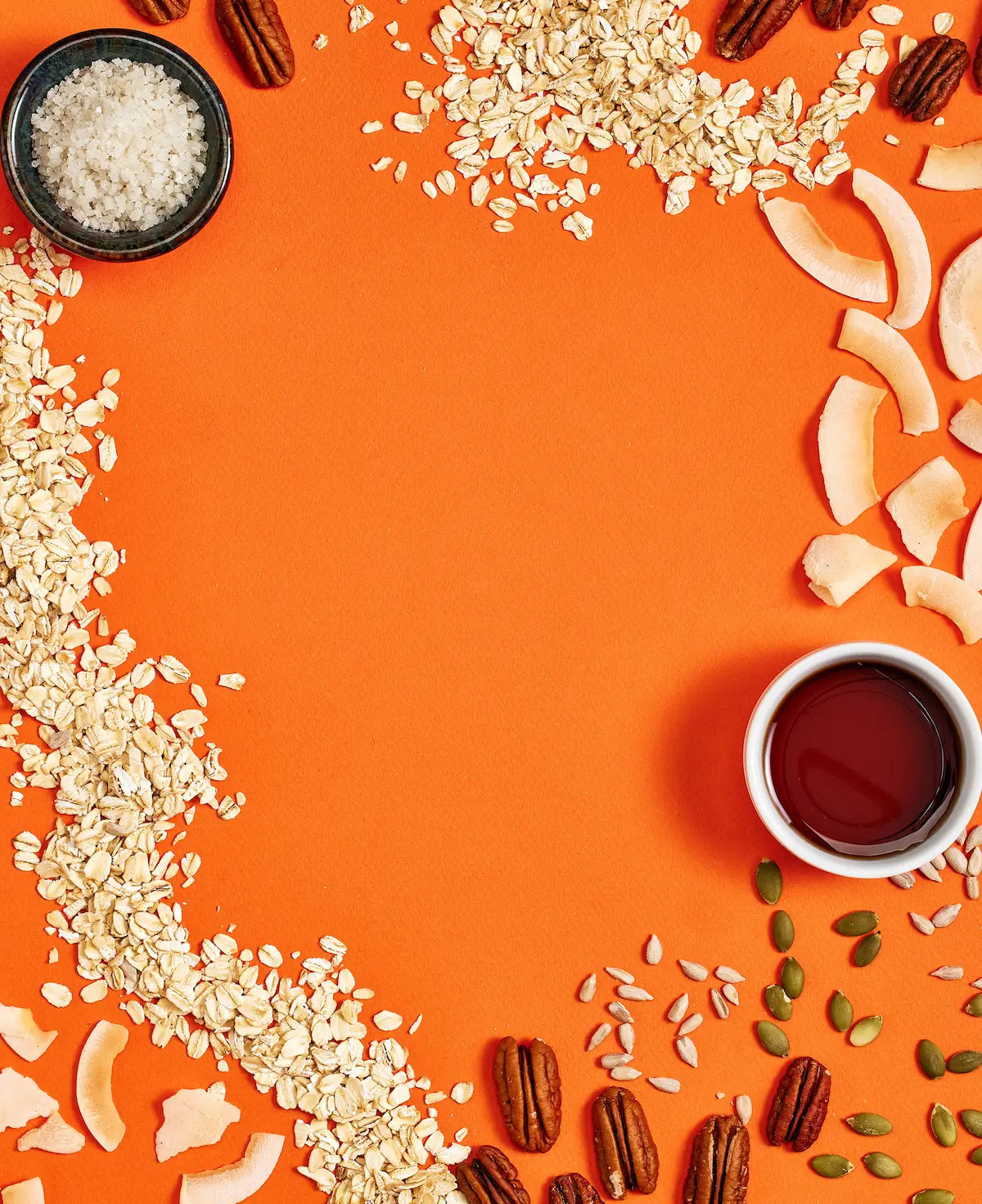 Michele's Granola assorted grains, nuts, and seeds arranged on an orange background with a small bowl of liquid in the center.