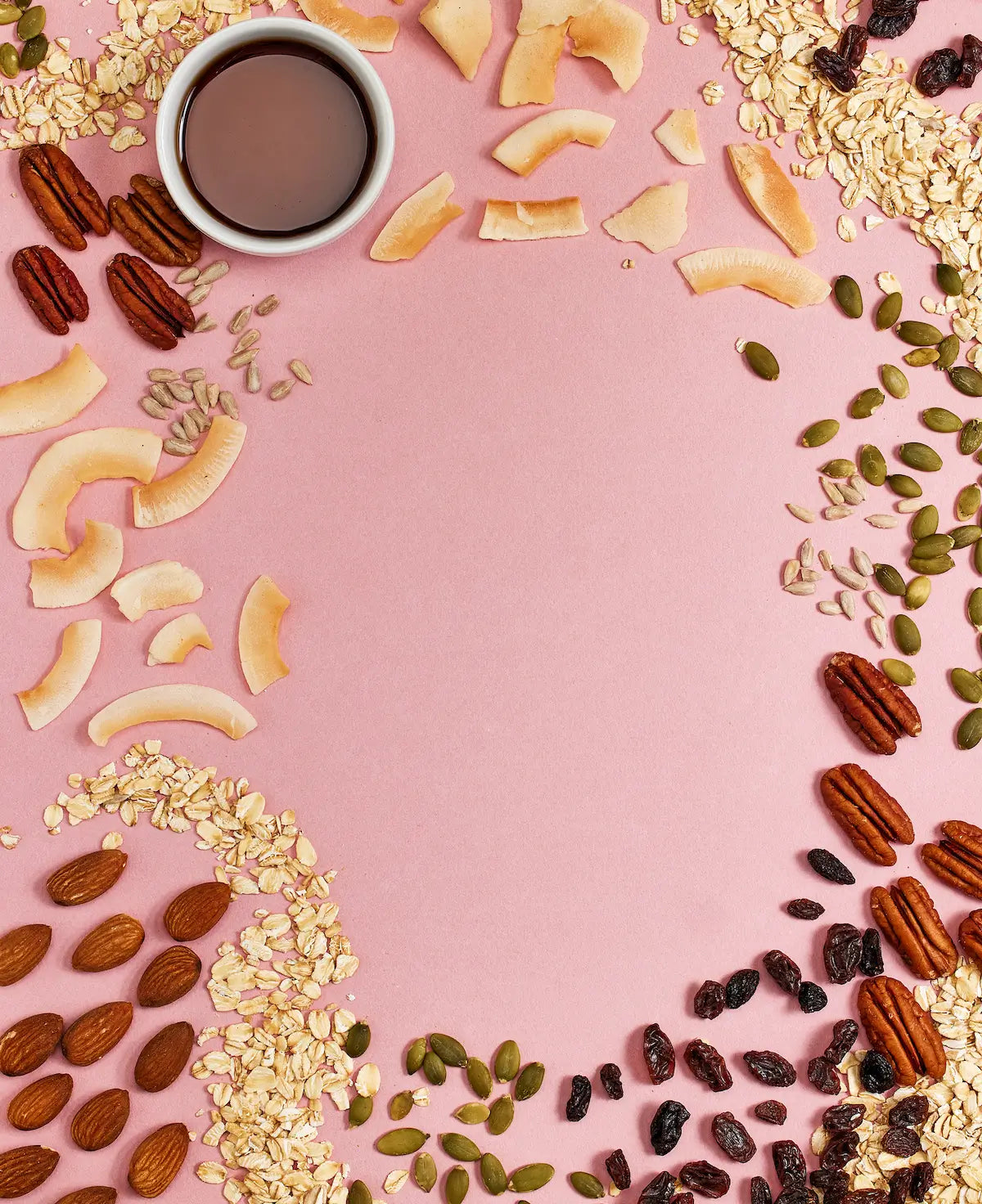 Michele's Granola nuts, seeds, and dried fruits arranged around a cup of coffee on a pink background