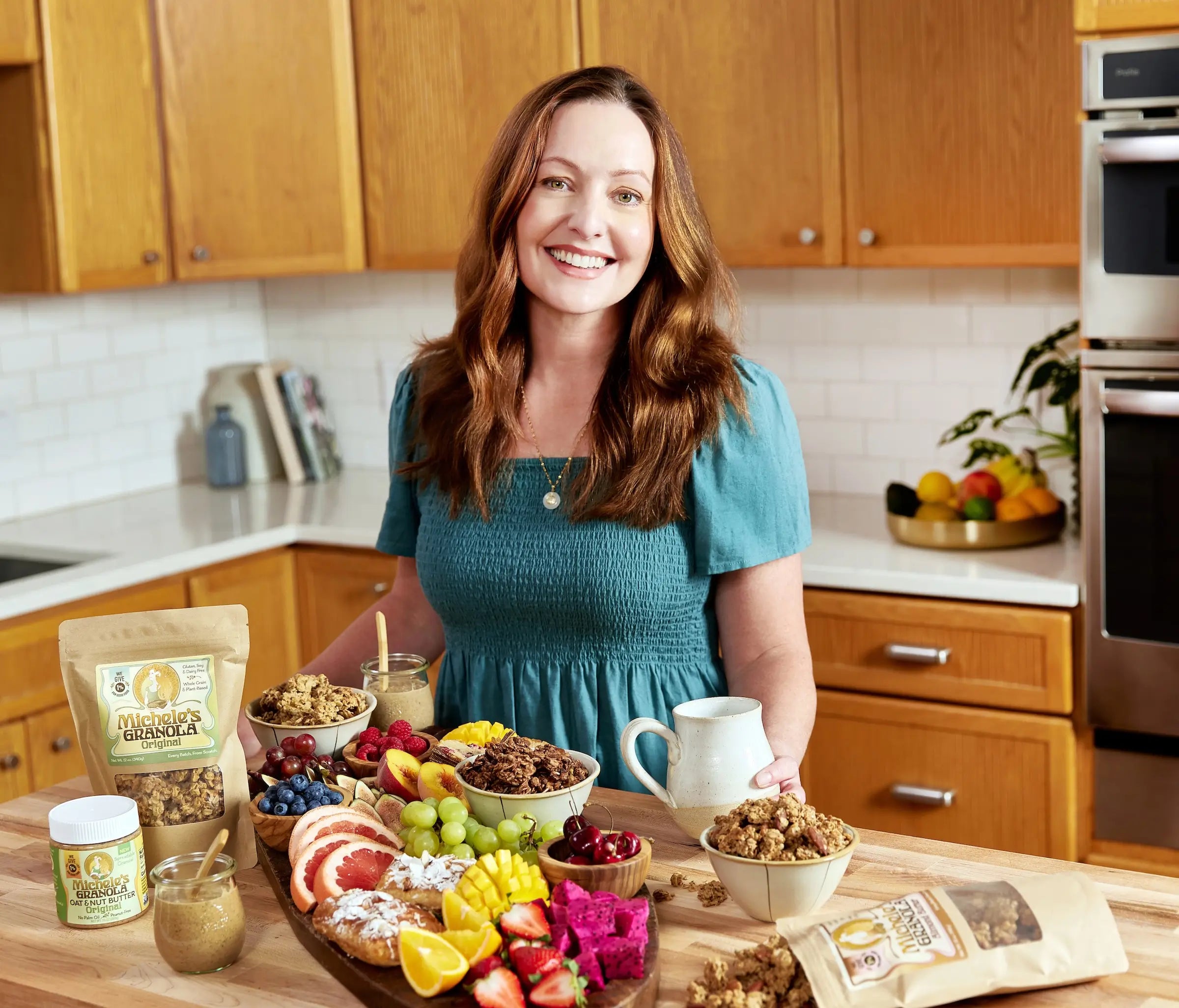 Michele (founder of Michele's Granola) in a kitchen with a table full of granola and fruits