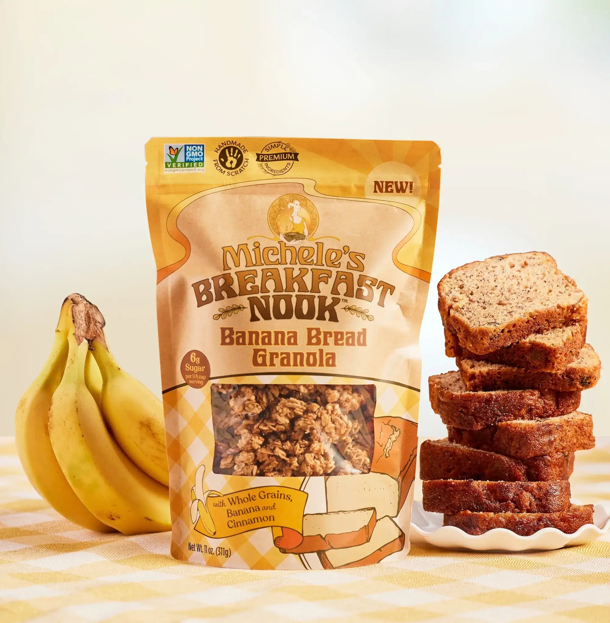 Michele's Breakfast Nook Banana Bread Granola package with banana bread slices and bananas on a striped tablecloth.