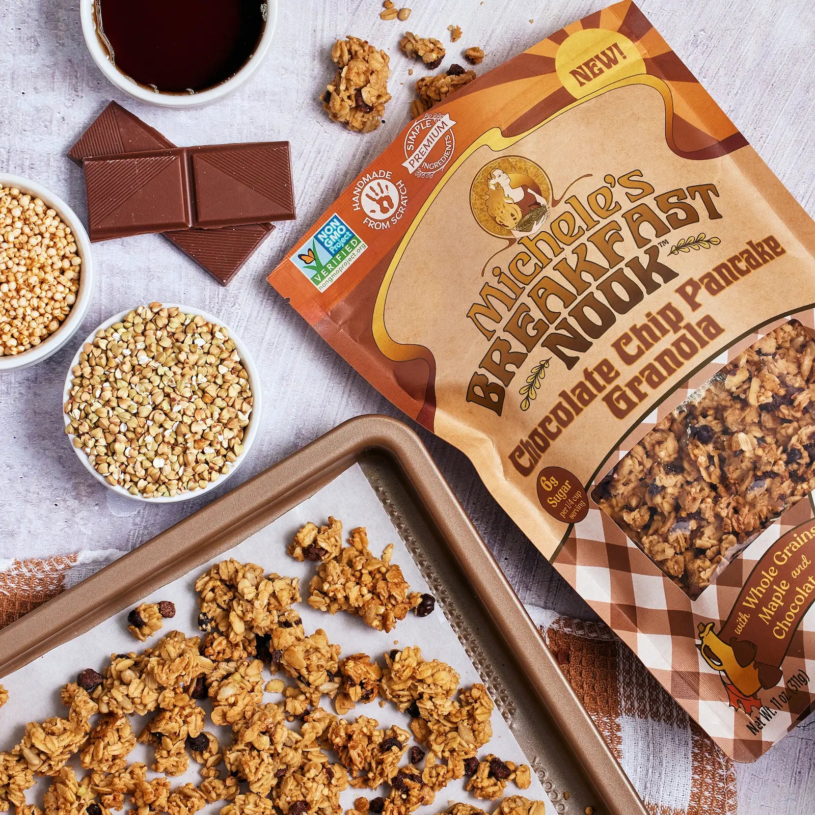 Michele's Breakfast Nook Chocolate Chip Granola on a baking sheet with ingredients and a cup of coffee.